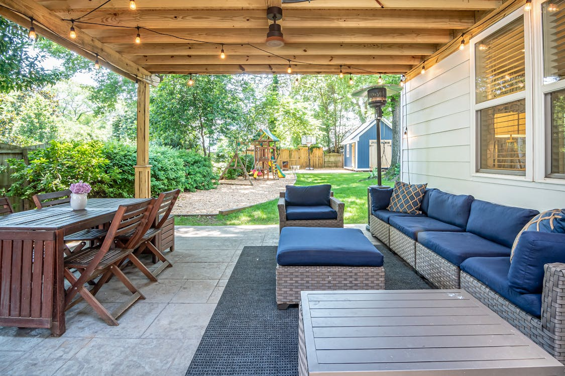 Covered outdoor living space with patio seating, dining area, string lights, and landscaping to increase home value.