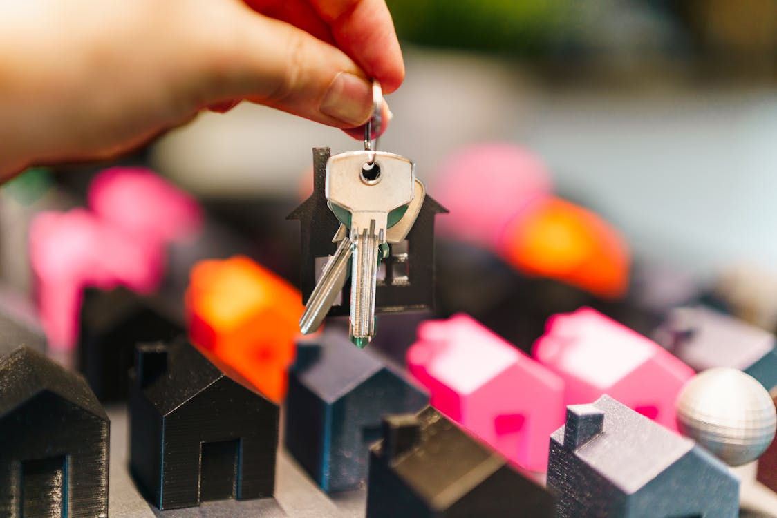 Hand holding house keys above miniature houses, symbolizing homeowner decisions in changing market.