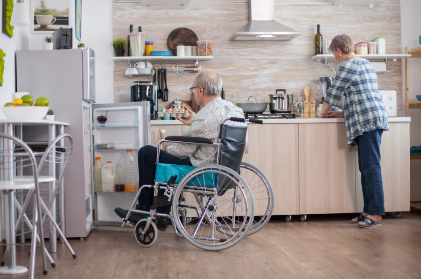 Older adult in a wheelchair accessing a refrigerator in an accessible, aging-in-place kitchen.